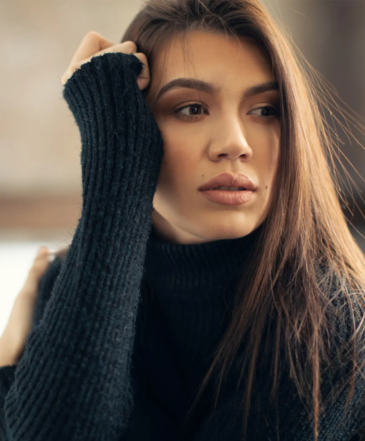 A beautiful woman with long, dark hair is looking away from the camera with a thoughtful expression. She is wearing a black turtleneck sweater and resting her hand on her head. - Dysport in Houston, TX